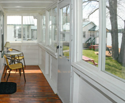 long view of porch with yellow chairs and small table, views of water, trees, and other cabins outside