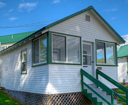 front exterior view of white cabin with green roof, stairs leading up to enclosed porch entrance