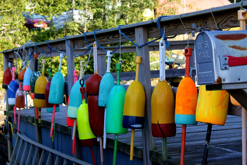 bright colorful lobster buoys are strung along a porch fence next to the mailbox