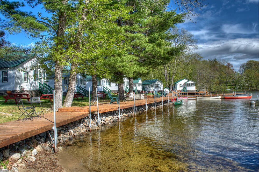 row of cabins and shoreline boat dock with pine trees and brilliant blue sky