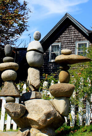 creative three-pronged rock sculpture in front yard of a weathered grey seaside cottage