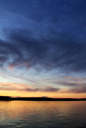 deep blue skies with long swirls of clouds reaching ground in orange twilight after sunset